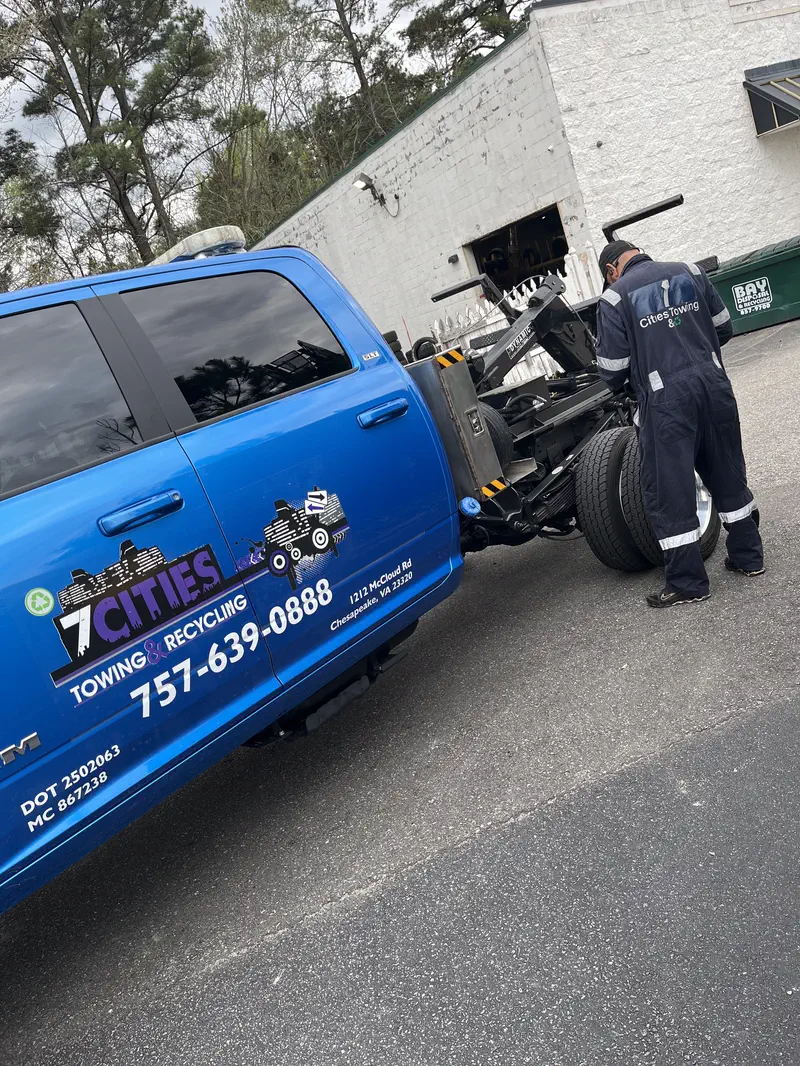 The blue 7 Cities truck, logo on the door, with the driver hooking up a cab-and-chassis behind it